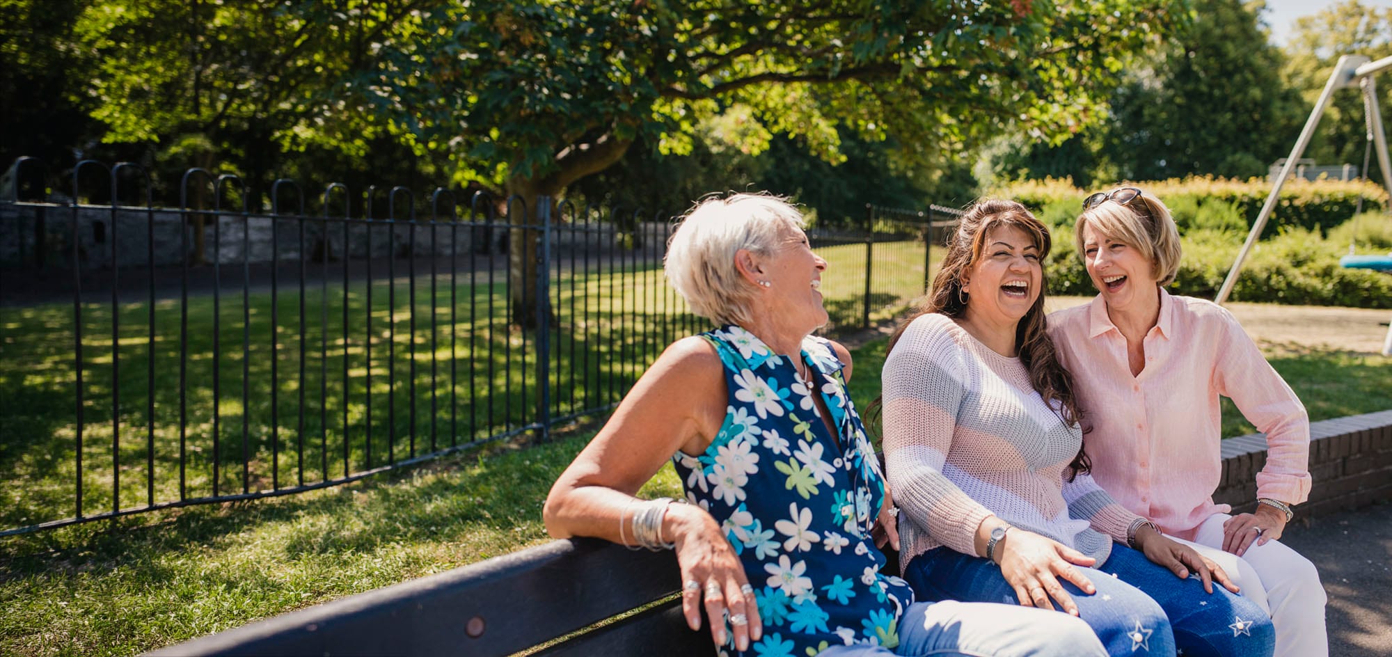 Middle aged ladies, laughing together on a park bench