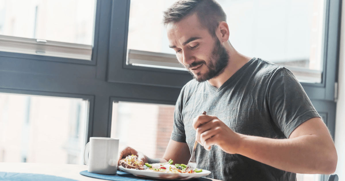 man with beard and short hair eating a healthy lunch with a mug